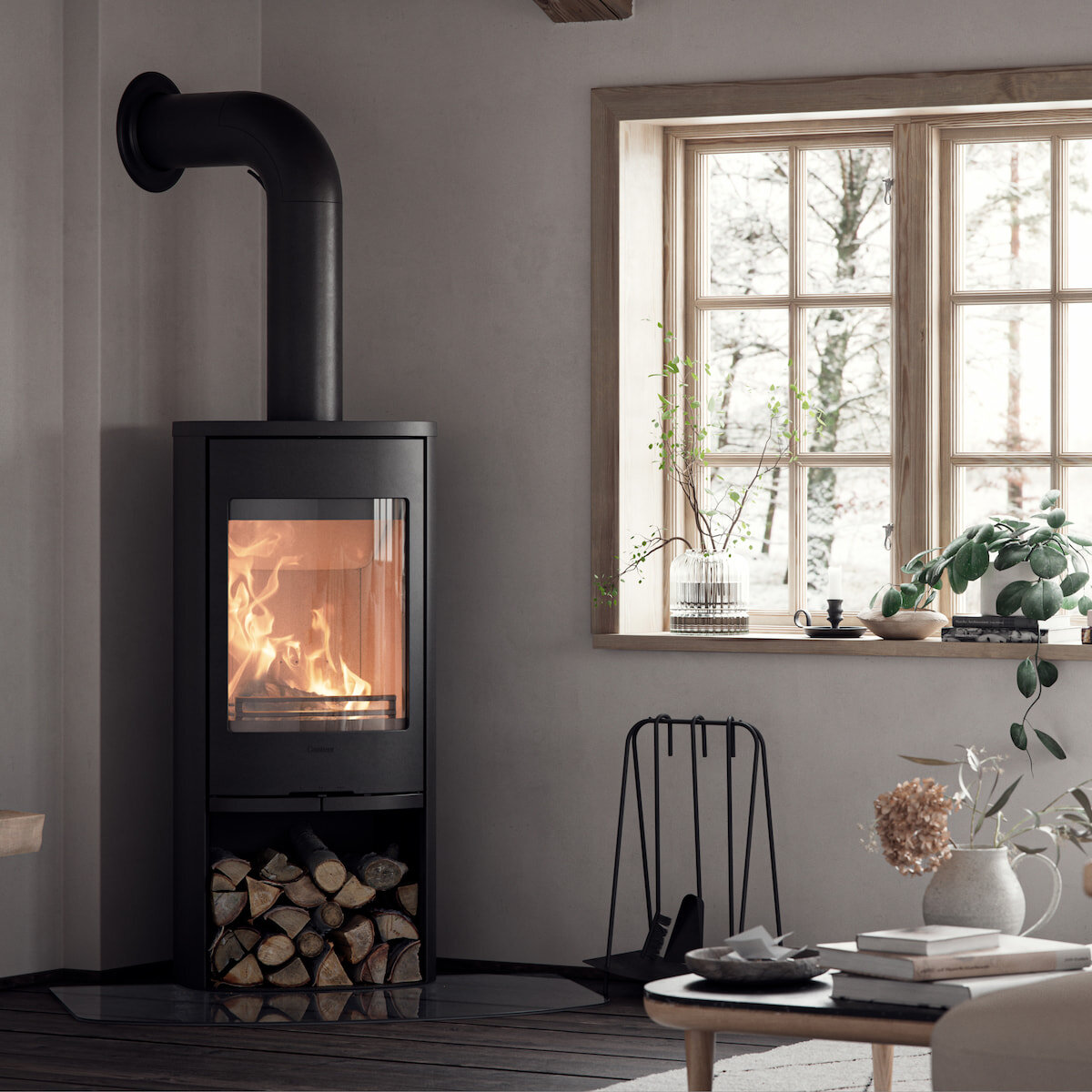 Klassisk svart vedovn med store glassflater med fyr i lys stue