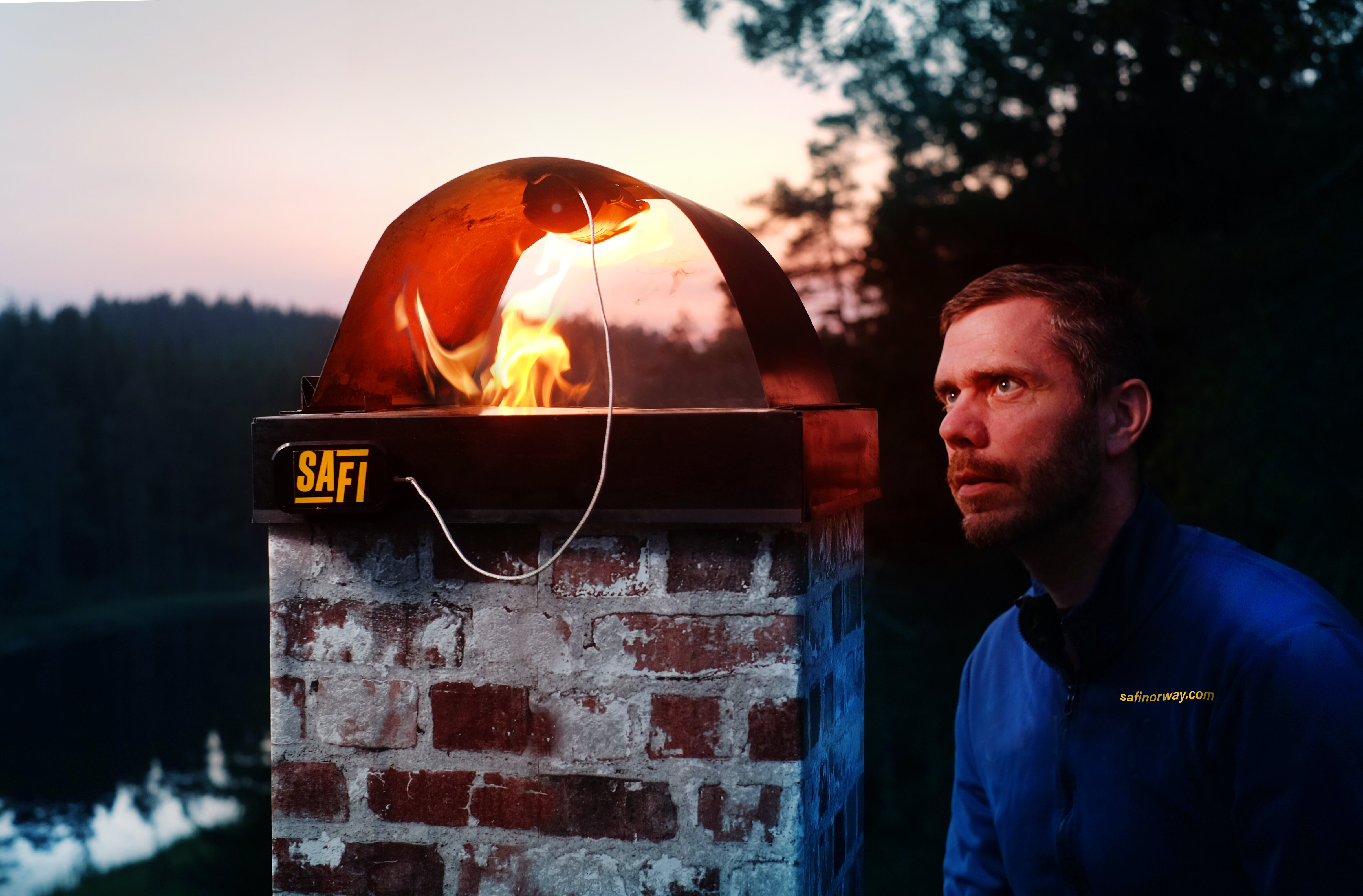 Safi Retro Fit i toppbuen på en pipe med Bildet som viser oppfinner av Safi pipebrannslukker ved siden av toppen av en pipe med pipebrann og Safi Retroi Fit festet i toppbuen på pipen