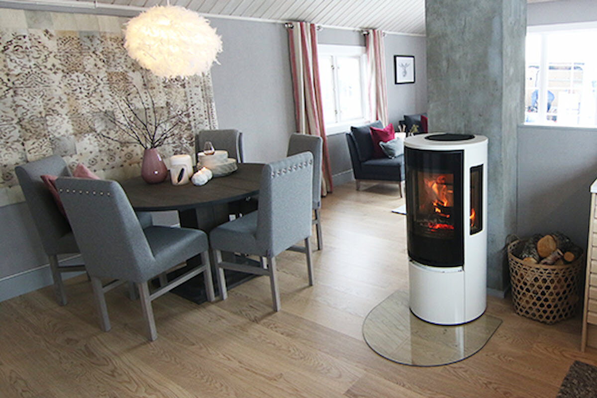 Hvit peisovn med glassdør med glassplate under plassert ved siden av spisebord