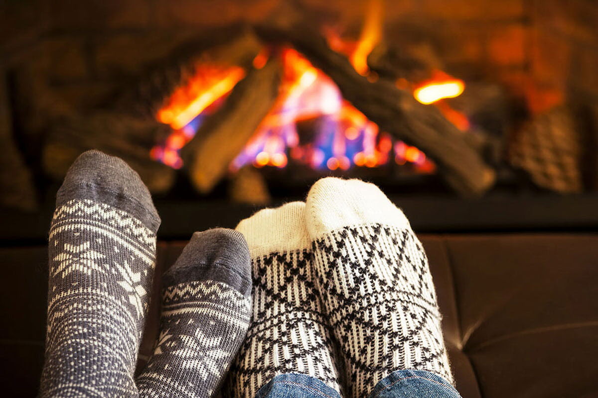 To par føtter iført sokker varmer seg foran peisen