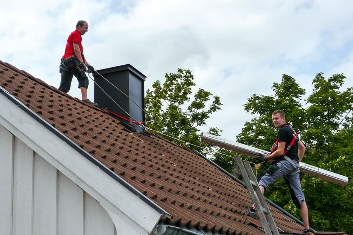 To menn fra Varmefag som jobber med piperehabilitering på taket til et hus