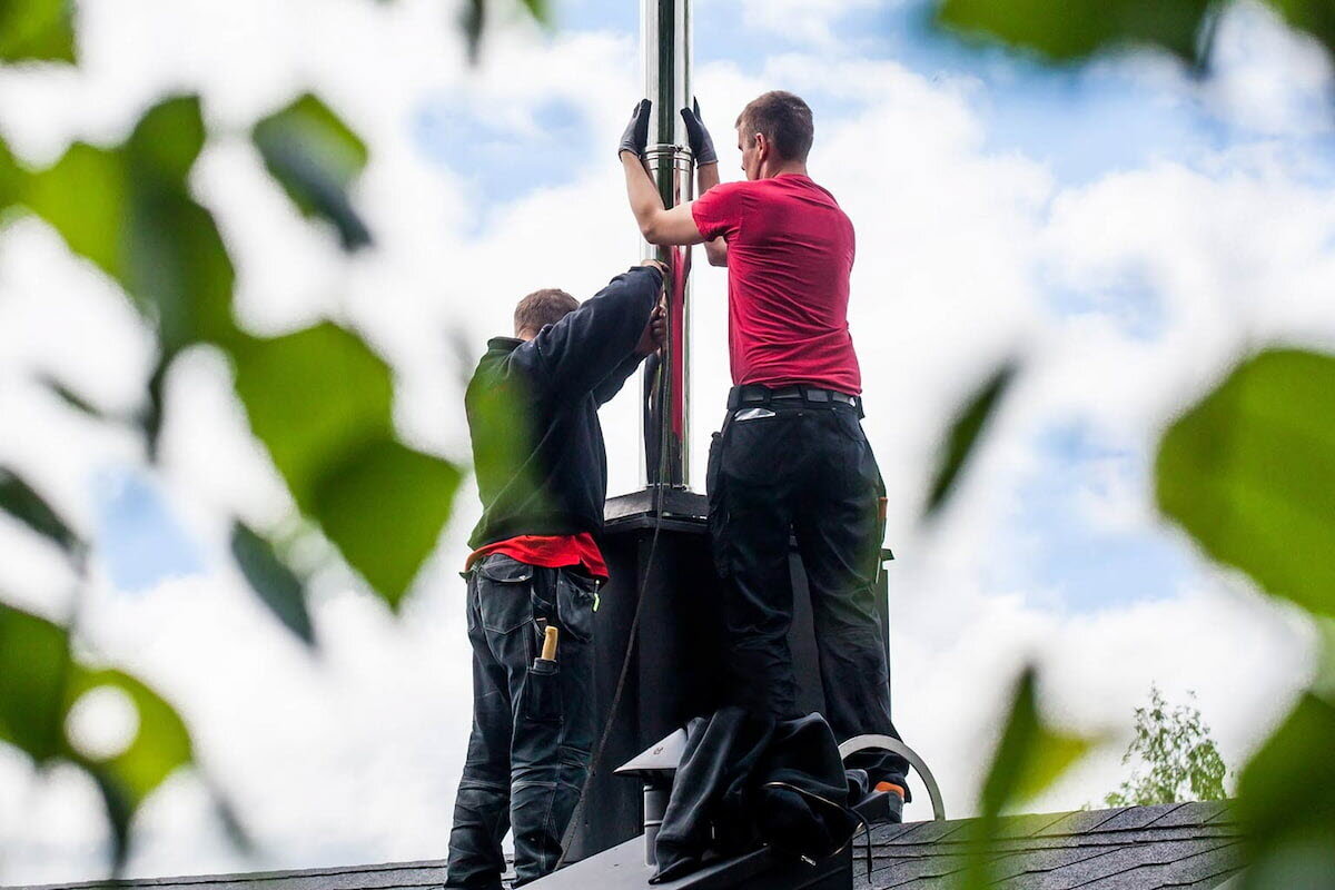 To menn som rehabiliterer en pipe på taket til et hus.