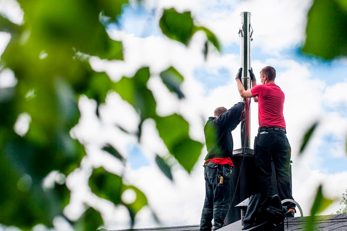 To menn fra Varmefag som installerer ny stålpipe på taket til et hus